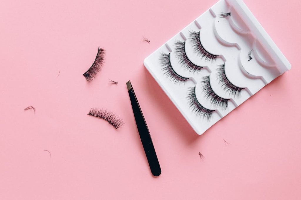 Multiple pairs of fake eyelashes and tweezers on a pink table